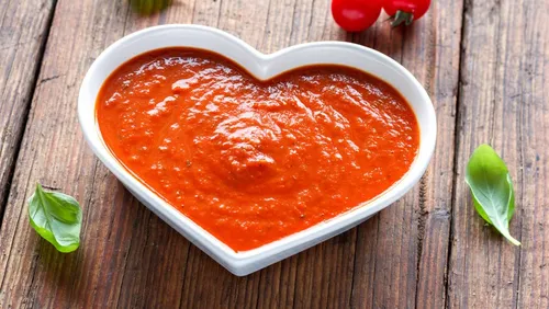 Heart shaped bowl with red sauce on wooden surface