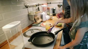 Pfanne mit Öl, während ein Kind sie mit Bürste bestreicht.