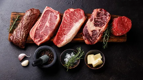 Pieces of meat lie on a wooden board with spices.