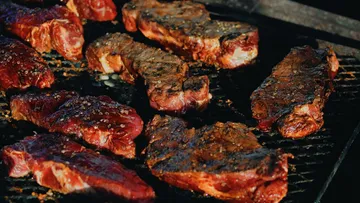 Pieces of meat sizzle on a grill under sunshine.
