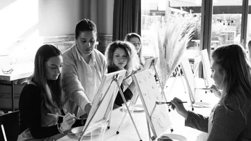 Female artists paint on easels in a bright room.