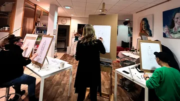 Three artists sketch figures in a studio.