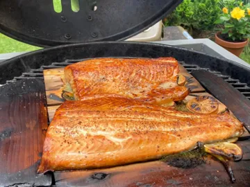 Lachsfilets grillen auf einer Holzplatte im Freien.