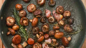 Champignons braten in einer Pfanne mit Kräutern.