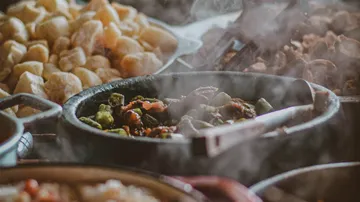 Ein Topf mit dampfendem Essen steht neben Beilagen.