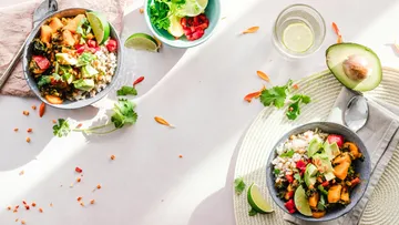 Two bowls of colorful vegetables and rice on table.