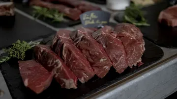 Raw meat is laid out on a table with fresh herbs.