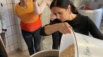 Frau gießt Malz in einen großen Kochtopf in einer Brauerei.