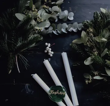 Three white candles lie between green leaves and branches.