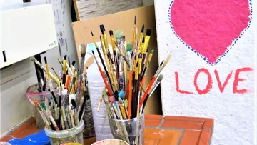 Pinsel stehen in Gläsern, neben einem `LOVE`-Graffiti.