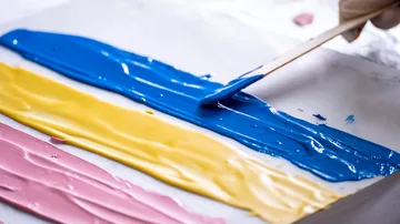 Paints on a surface are spread with a spatula.