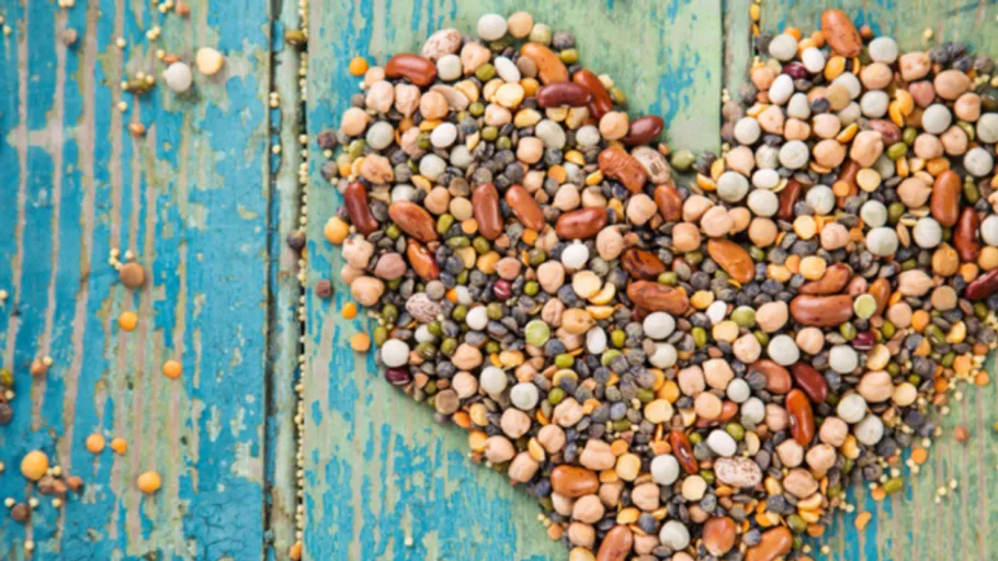 Heart-shaped pattern of mixed beans on wood.
