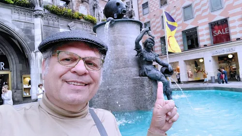 Man points at fountain with statue in an urban environment.