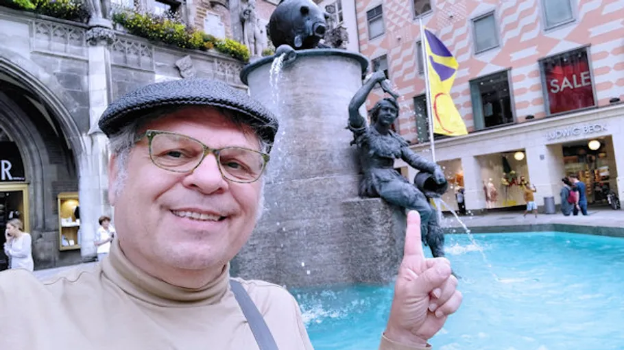 Mann zeigt auf Brunnen mit Statue in urbanem Umfeld.