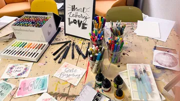 Paints and markers are on an artist's table for design.