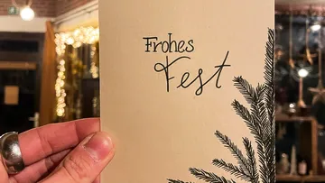 One hand is holding a card with “Happy Holidays.”