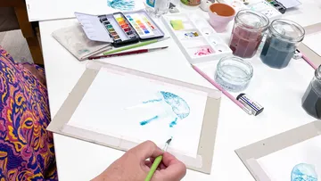 Person paints a jellyfish on paper with watercolors.