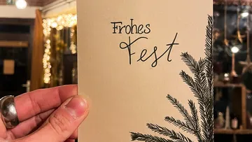 Hand holding a card with “Happy Holidays” and pine branches.