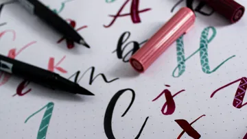 Pens lie on a sheet of colorful letters.