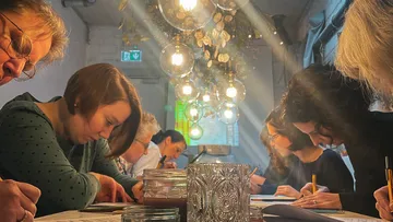Participants write concentrated at a table in a bright room.