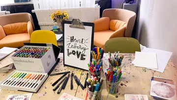 Bunte Stifte liegen auf einem Tisch, beschriftet mit „Handlettering LOVE“.