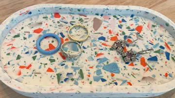 Bunte Schmuckstücke liegen auf einer marmorierten Schale.