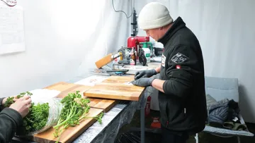 Mann schneidet Lebensmittel auf einem Holzbrett in einer Küche.