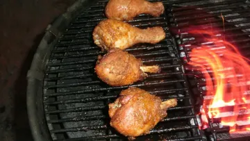 Hähnchenstücke brutzeln auf einem Grill über offenem Feuer.
