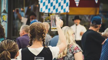 Frau hebt Bierkrug beim Feiern in einer Menschenmenge.