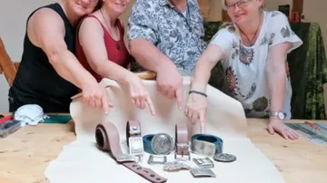 Vier Personen zeigen auf mehrere Gürtel auf einem Tisch.