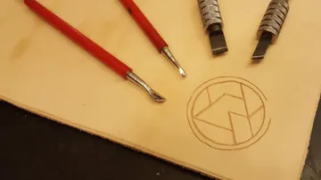Werkzeuge liegen neben einem eingeprägten Logo auf Leder.
