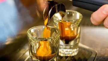 Espressomaschine gießt Kaffee in zwei Gläser. Hintergrund verschwommen.