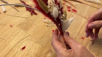 Hands tie dried flowers together on a wooden table.