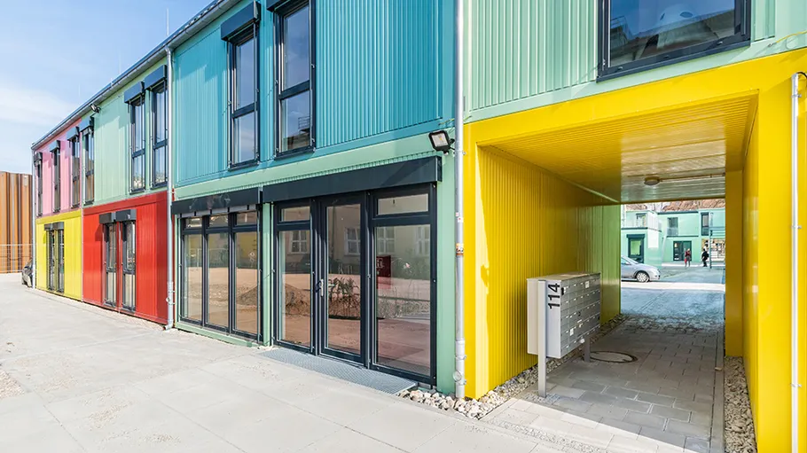 Bunte Wohngebäude mit Eingang, umgeben von Straßen und Pflanzen.