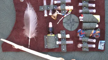 Object: Various small containers and tools. Action: Arrangement on a surface. Context: Natural-colored felt and a feather next to it.