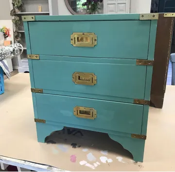 Blue dresser with three drawers stands on a table.