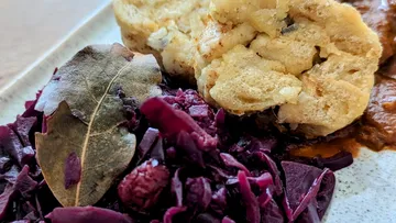 Rote Kohl, Klöße und Sauce auf einem Teller serviert.