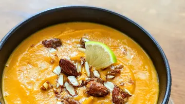 Orangefarbene Suppe mit Mandeln und Limettenscheibe dekoriert.