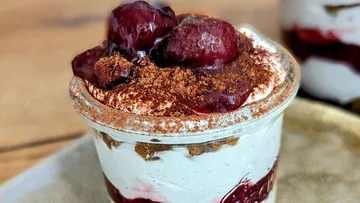Dessert im Glas mit Kirschen und Kakao-Pulver obendrauf.