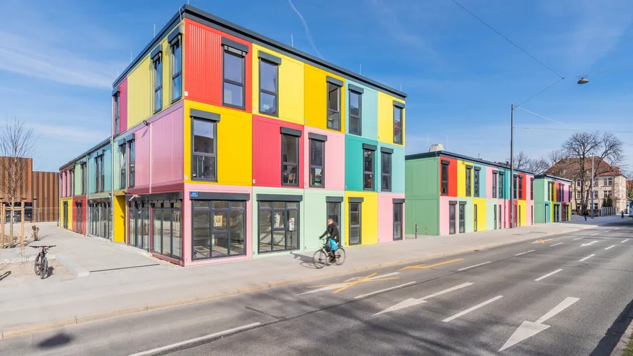 Colourful building, cyclists ride along a road.