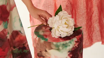 Eine Hand legt eine künstliche Blume auf einen Hocker.