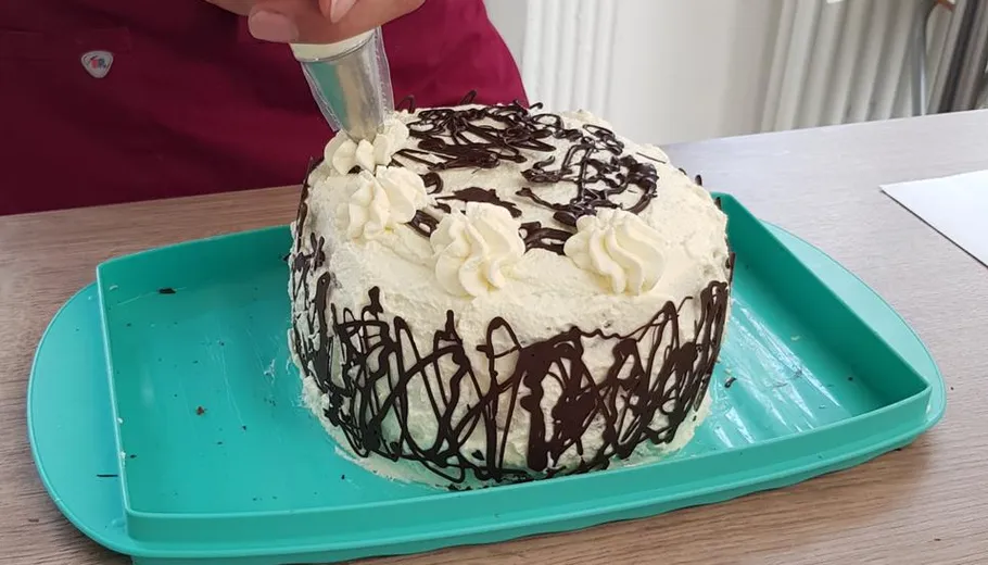 Person, die einen Kuchen mit Zuckerguss auf dem Tablett dekoriert.