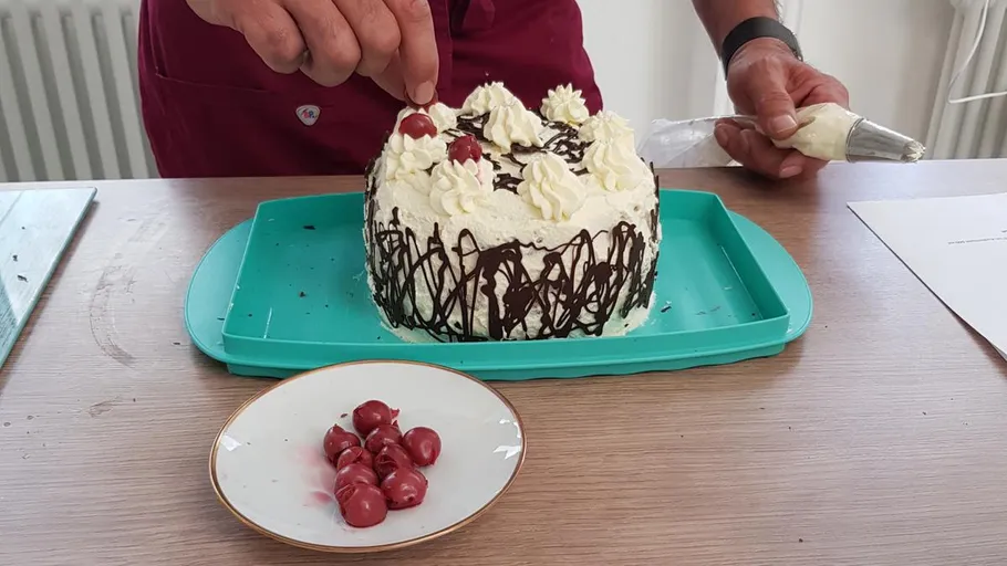 Person, die Kuchen mit Kirschen und Sahne dekoriert.