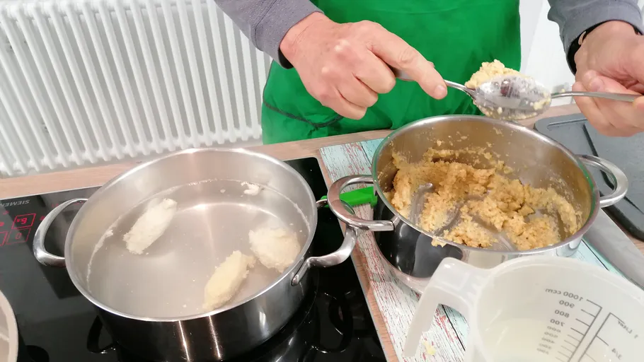 Ein Koch formt Teigbällchen, um sie ins Wasser zu geben.