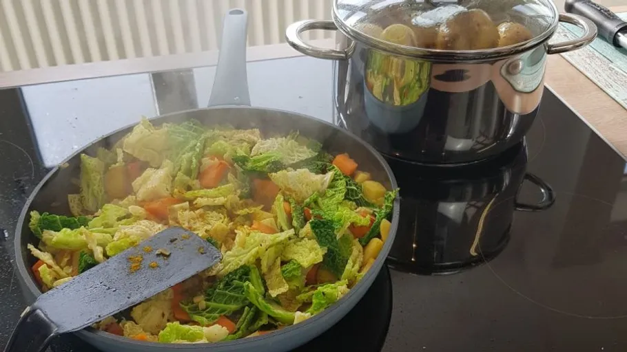 Gemüse brät in einer Pfanne, daneben ein Topf mit Kartoffeln.