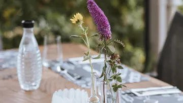 Eine Glasflasche mit Blumen dekoriert einen Tisch im Freien.
