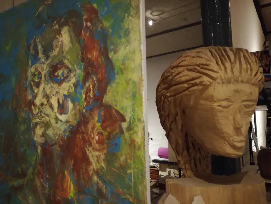 Paintings and wooden sculptures stand side by side in a room.