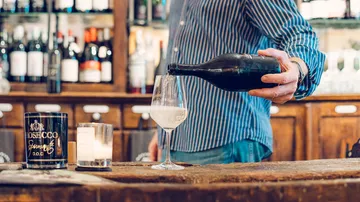 Glass is filled with prosecco at a wooden bar.