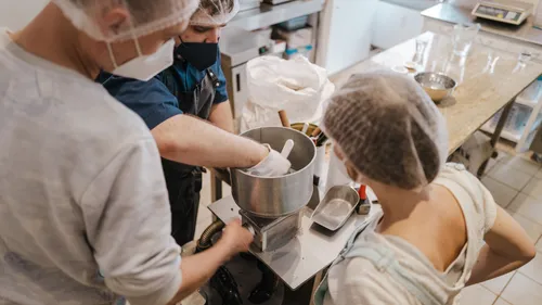 Three people work together on a machine in the kitchen.