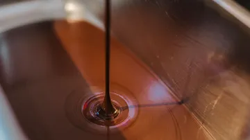 Dark chocolate flows into a metal bowl.